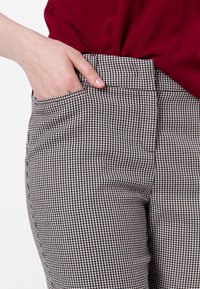 Un pantalon à motif pied-de-poule noir et blanc qui présente une taille plate à l'avant et des poches latérales, avec une texture lisse et une coupe ajustée.
