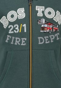 Groene rits hoodie met "BOSTON 23/1 FIRE DEPT." geborduurd. Bevat een grafiek van een brandweerwagen, gele rits en voorzakken.