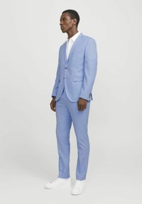 Light blue suit with slim fit, single-breasted jacket and flat-front trousers, paired with a white shirt and white sneakers.