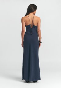 Navyblaues Maxikleid mit tailliertem Oberteil und offenem Rücken. Mit dünnen, verstellbaren Trägern und einer Schleifen-Applikation auf der Rückseite. Glattes, fließendes Material.