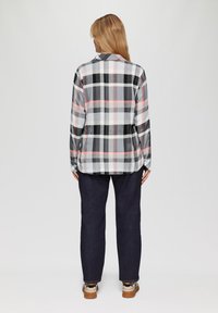 Geruit flanellen overhemd in grijs, zwart, wit en roze met knoopsluiting, lange mouwen en een casual pasvorm, gecombineerd met donkere jeans en sneakers.