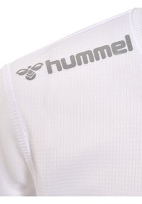T-shirt de sport blanc avec un tissu texturé. Présente un logo "hummel" gris et un emblème d'abeille sur l'épaule, mettant en valeur leur identité de marque.