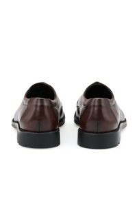 Zapatos de cuero marrón con un acabado suave, punta redondeada y un ligero tacón. Suela de goma negra. Detalles de costura a lo largo de los lados.