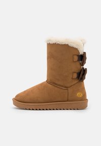 Bottine en suède marron avec doublure en fausse fourrure et deux nœuds latéraux. Dotée d'une semelle en caoutchouc plate et striée avec des détails cousus.