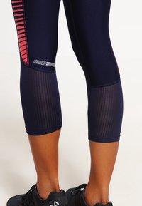Námořnické sportovní legíny s síťovinovými panely, s růžovými pruhy a logem Under Armour, navržené pro pohodlí a pohyblivost.