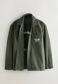 Grüne, knöpfbare Jacke aus Baumwolle mit weit geschnittenem Schnitt. Sie hat eine Brusttasche, ein gesticktes "PORTLAND"-Logo und einen flachen Kragen.