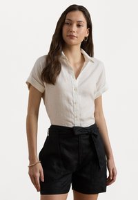 Light beige linen button-up shirt with rolled sleeves, paired with black high-waisted shorts featuring a belted waist and side pockets.