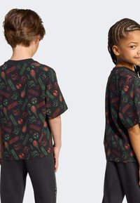 Čierne tričko s krátkym rukávom s farebnými vzormi Disney a športovými motívmi, s voľným strihom a okrúhlym výstrihom. Skombinované s čiernymi nohavicami.