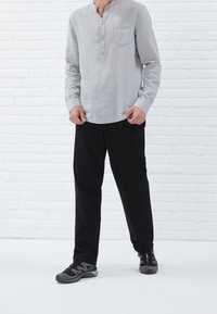 Grijze linnen overhemd met lange mouwen, een knopenlijst en een zak, gecombineerd met zwarte broeken en grijze sneakers. Eenvoudige, casual outfit.