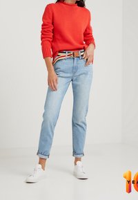 Maglione a coste rosso, jeans azzurri a vita alta con risvolti, e sneakers bianche. Cintura marrone e a righe aggiunge contrasto.