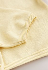 Lysegul strikket sweater med ribbede manchetter og kant. Materialet er blødt med en glat tekstur og har et enkelt, afslappet design.