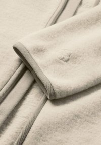 Hellbeige Pullover mit weicher Textur, ausgestattet mit einem gerippten Kragen und Bündchen. Ein kleines gesticktes Logo befindet sich am Ärmel.