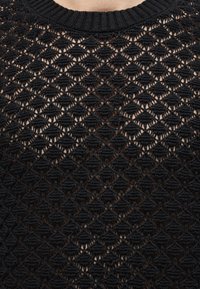 Μαύρο πλεκτό πουλόβερ με ανοιχτό μοτίβο ραφής σε σχήμα ρόμβου που αποκαλύπτει το δέρμα από κάτω, με ριμπ στρογγυλή λαιμόκοψη.