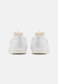 Vita sneakers med en slät, matt yta och en pluffsig ljusrosa blommaaccent bak. Lågt profil design med rundade kanter.