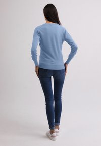 Ljusblå tröja i stickad tyg, med långa ärmar och rundad halsringning, kombinerad med mörkblå skinny jeans och vita sneakers.