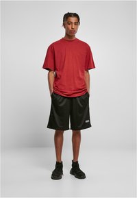 Tricou roșu din bumbac cu mâneci scurte, asortat cu șorturi negre din plasă. Modelul poartă pantofi sport negri. Îmbrăcăminte sport simplă și lejeră.