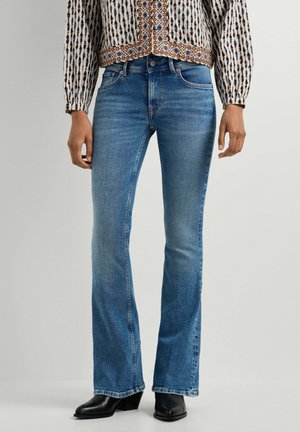 Slim fit blå jeans med let vidde, kombineret med sorte hælede støvler og en mønstret langærmet top.