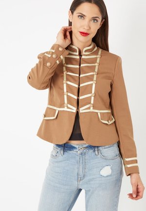 Chaqueta de estilo militar marrón con detalles en oro, cuello alto y botones decorativos. Presenta dos bolsillos frontales y un diseño ajustado.