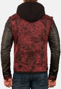 Giacca in denim rossa e nera con maniche in pelle, tessuto strappato, dettagli con borchie lungo le cuciture e design con cappuccio.