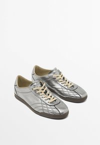 Baskets argentées en matériau synthétique métallique avec une texture matelassée, dotées de lacets beige et d'une semelle en caoutchouc.