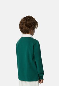 Camisa verde de manga larga con cuello blanco, que presenta una textura suave y aberturas laterales, vista desde la parte trasera.