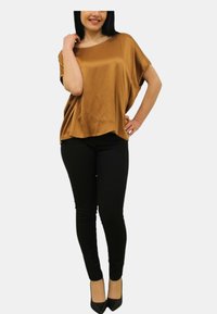 Top in satin bronzo con una vestibilità ampia e scollatura larga, abbinato a pantaloni skinny neri e tacchi a punta neri.