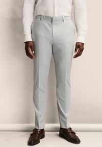 Pantalones de traje gris claro con una textura suave, corte recto y dos bolsillos frontales. Combinados con zapatos de cuero marrón.