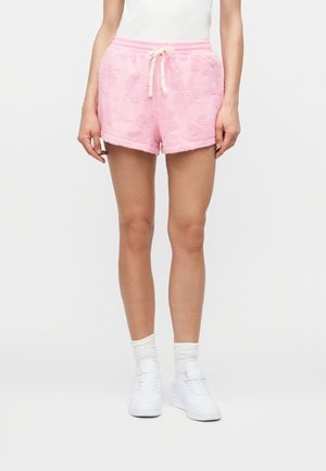 Personne portant un short rose texturé à motifs floraux avec un cordon de serrage crème, des chaussettes blanches, des baskets blanches et un haut blanc sans manches.