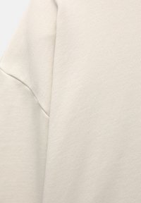 Lichtbeige sweatshirt van een gestructureerde stof, met een ontspannen pasvorm en verlaagde schoudernaden, wat een gladde, matte afwerking benadrukt.