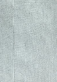 Tessuto intrecciato grigio chiaro con una superficie testurizzata, caratterizzato da un motivo sottile di piccoli fili uniformemente distanziati. Dettaglio della cucitura visibile.