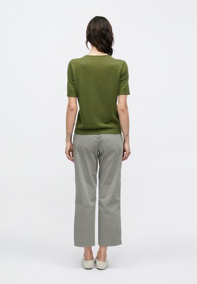 Πλεκτό με κοντά μανίκια σε ελιά πράσινο και ανοιχτό γκρι παντελόνι με φαρδιά γραμμή. Λείο υφασμάτινο, απλός σχεδιασμός και κλασική εφαρμογή. Τα παπούτσια είναι σε ανοιχτό χρώμα.