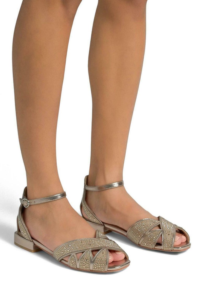 Open-toe sandalen met een metallic beige afwerking, versierd met strassteentjes, een platte hak en een enkelbandje met een gespsluiting.