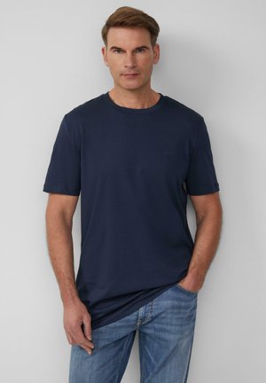 Navyblaues T-Shirt mit kurzen Ärmeln aus weichem Material, mit einem Rundhalsausschnitt und minimaler Markenkennzeichnung auf der Brust, kombiniert mit hellblauen Jeans.