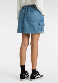 Farkuhame, joka on varustettu joustavalla vyötäröllä, kahdella takataskulla ja sivutaskulla. Vaalea sininen väri, polvipituus ja rento muotoilu.