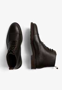 Botas de tobillo de cuero negro con acabado texturizado, punta redonda y diseño con cordones. Presenta ojales de bronce y una suela de goma marrón.