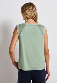 Grön ärmlös topp i ett mjukt tyg med en enkel design, med meshdetaljer på axlarna och en rak nederkant.