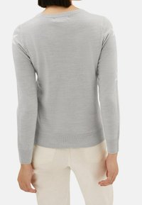 Femme portant un pull léger gris à manches longues avec ourlet et poignets côtelés, associé à un pantalon blanc cassé, vue de dos.