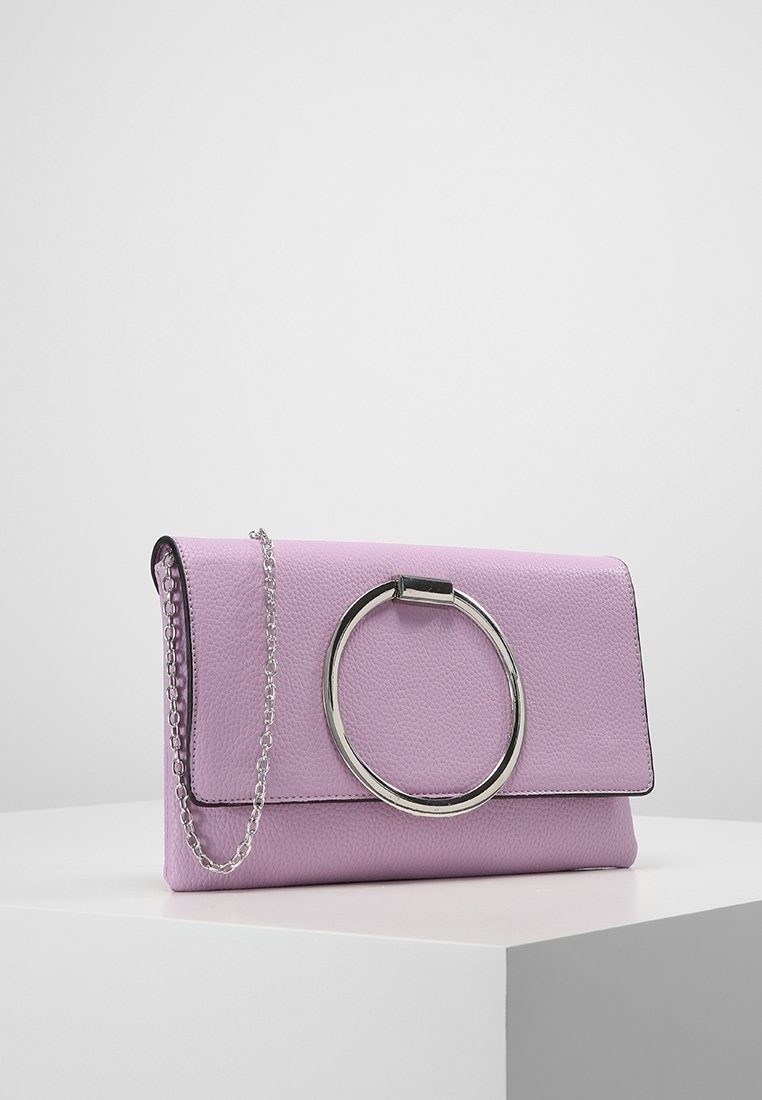 Pochette en cuir structuré lilas avec une grande poignée circulaire argentée et une fine bandoulière chaîne argentée reposant sur une surface blanche.