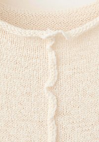 Gros plan sur un tissu tricoté couleur crème avec un détail de volants verticaux au centre et un motif texturé.
