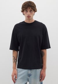 T-shirt nera oversize con maniche corte, collo a giro e una texture liscia. Indossata con jeans di denim azzurri.