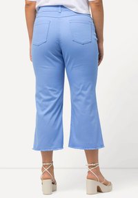 Vaaleansiniset lyhennetyt housut, joissa on purjehtiva helma ja kaksi takataskua, valmistettu pehmeästä kankaasta. Yhdistetty vaaleanbeigeihin paksu-arkin sandaaleihin.