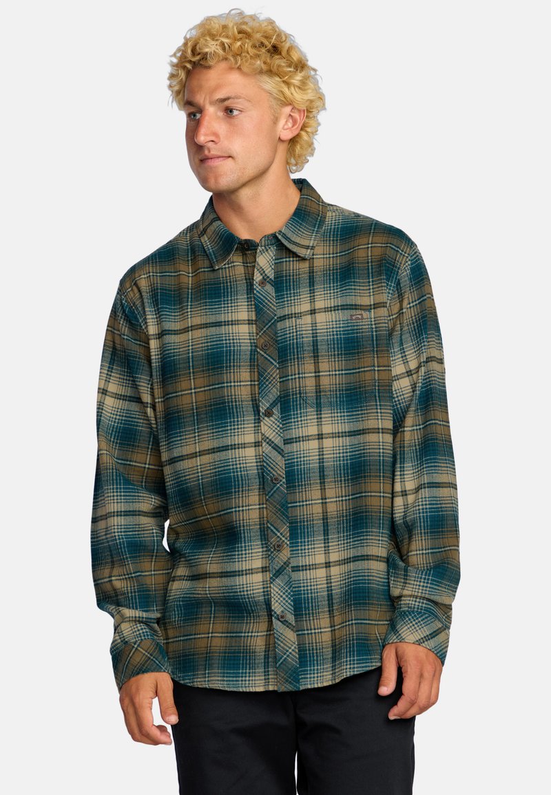 Camicia flanella a bottoni in un motivo a quadri blu e marrone. Realizzata in un tessuto morbido con maniche lunghe e colletto. Presenta bottoni scuri.