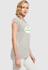 Pilkos medvilninės marškinėliai trumpomis rankovėmis, turintys apvalų kaklą ir mėlyna apvadu ovalų logotipą su užrašu "Gilmore girls."