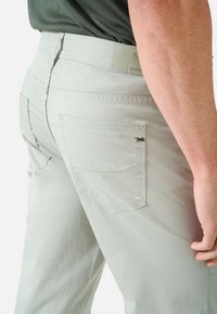 Lichtgrijze broek met een gladde textuur, voorzien van achterzakken en subtiele stiksels. De tailleband heeft een logo-tag met "ULTRA-LIGHT" geprint.