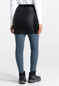 Schwarzer gepolsterter Skort mit strukturierter Oberfläche, kombiniert mit enganliegenden grauen Leggings. Die Schuhe haben ein grau-schwarzes Design mit pinken Akzenten.