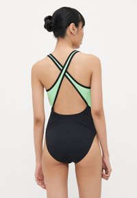 Maillot de bain avec un bas noir et un haut vert menthe à bretelles croisées ; texture lisse avec un minimum de détails et un dos échancré.