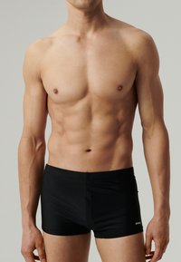 Czarne szorty do pływania wykonane z gładkiego, elastycznego materiału o dopasowanym kroju. Pas jest elastyczny, z małym logo z boku.