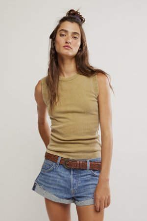 Giovane donna con lunghi capelli castani raccolti in un mezzo chignon, che indossa un top beige senza maniche, cintura marrone intrecciata e pantaloncini di jeans blu.