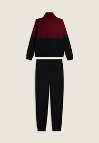 Felpa a maniche lunghe, bicolore bordeaux e nera abbinata a pantaloni jogger neri su uno sfondo beige.