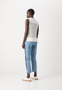 Pantavilla beige avec des rayures horizontales bleu marine, associée à un jean bleu clair avec un panneau latéral bleu foncé, et des baskets blanches avec des semelles beige.